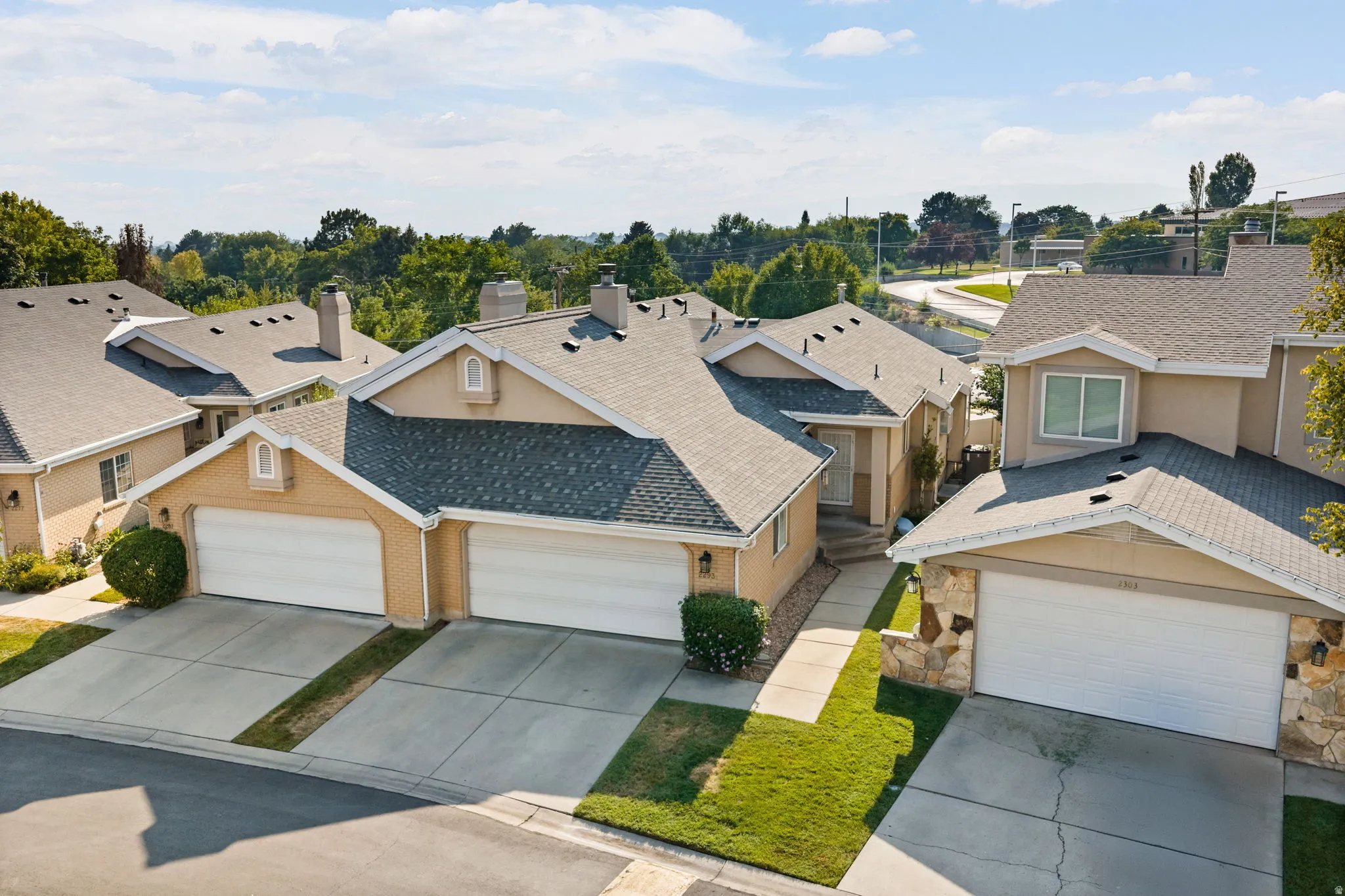Multi-unit property with tan exterior siding, pitched shingle roofs, and attached garages