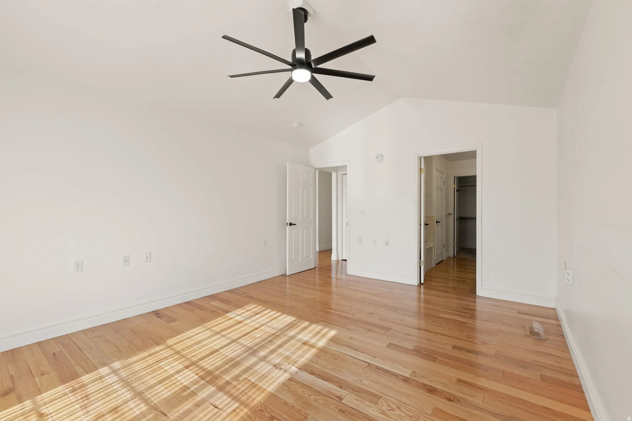 Vaulted ceiling, wood-finish flooring, white walls, black ceiling fan with integrated lighting, and white paneled doors