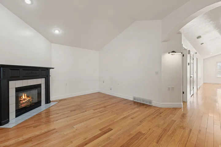 Hardwood flooring, recessed lighting, vaulted ceiling, tile-surround fireplace with mantel, and arched doorway