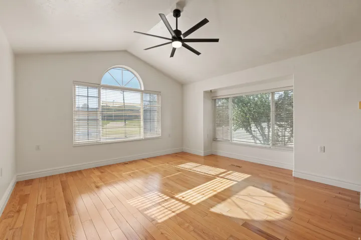 Vaulted ceiling with a black ceiling fan, wood-finish flooring, and multiple large windows with blinds