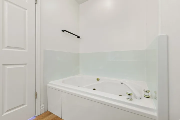Corner jetted bathtub with a white finish, featuring a glass partition and gold-tone fixtures