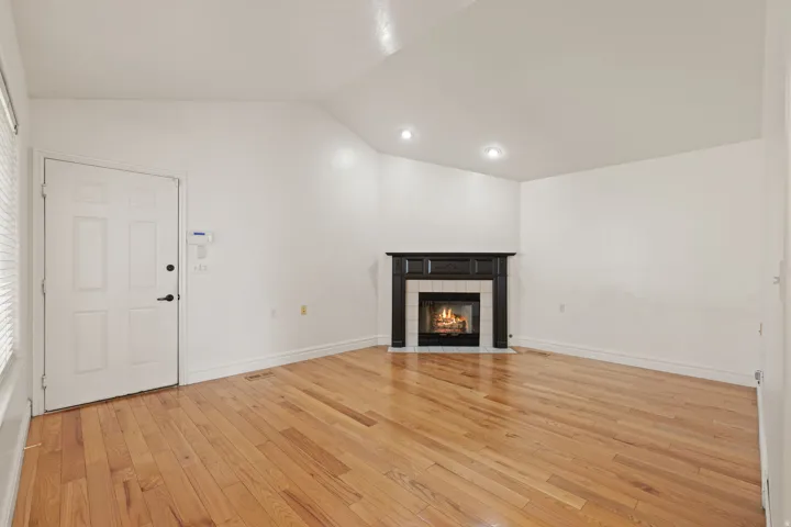Hardwood flooring, corner fireplace with dark wood-finish mantel, vaulted ceiling, and recessed lighting