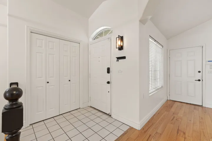 Entryway featuring a vaulted ceiling, wood-finish flooring, white paneled doors, and a decorative arched transom window