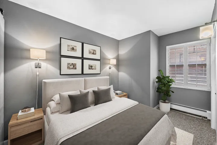 Wall-mounted sconce lighting, window with white plantation shutters, light gray wall finish, and neutral-toned carpeting