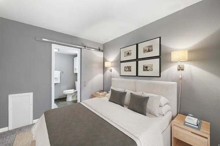 Barn door entry, wall-mounted sconce lighting, upholstered headboard, and wood-finish nightstands