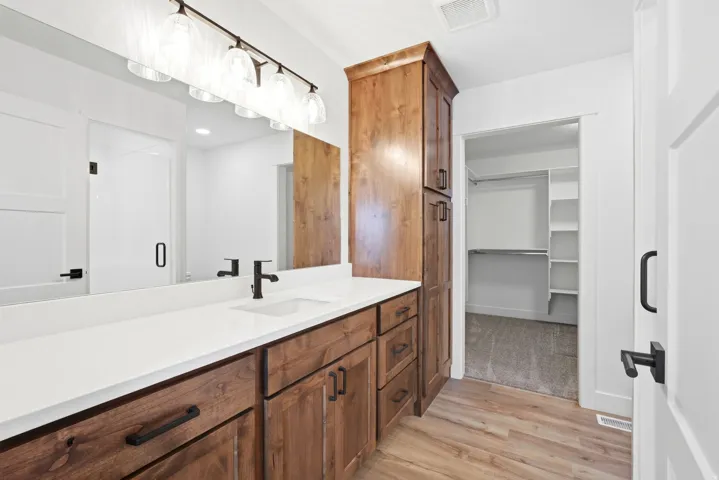 Wood-finish flooring with a vanity featuring a white countertop, undermount sink, and dark-toned cabinetry