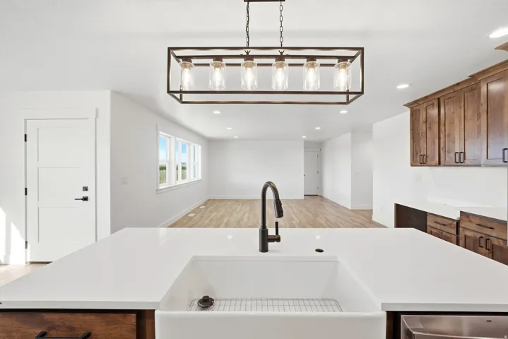White farmhouse sink with a matte black pull-down faucet, white countertop, and dark wood-finish cabinetry