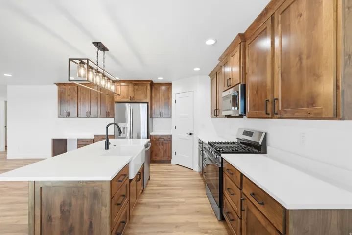 Kitchen featuring wood-finish flooring, an expansive island with a farmhouse sink, stainless steel appliances, and wood cabinetry with matte black hardware