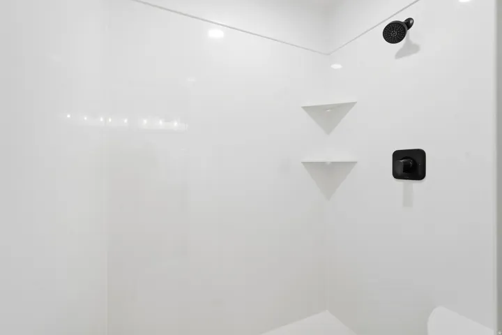 Shower enclosure featuring a matte black shower head, matte black controls, and built-in corner shelving