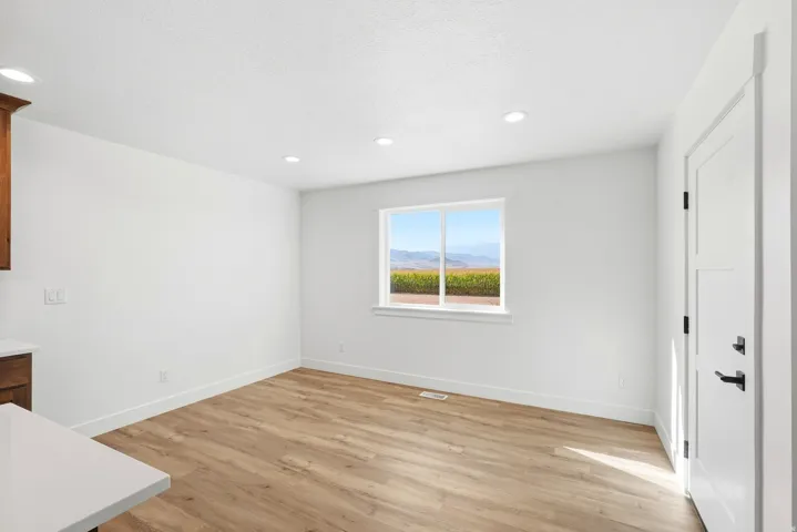 Recessed lighting, wood-finish flooring, white walls, white trim, and a white interior door with matte black hardware