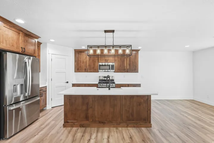 Kitchen featuring wood-finish cabinetry, stainless steel appliances, a center island with white countertop, and wood-finish flooring