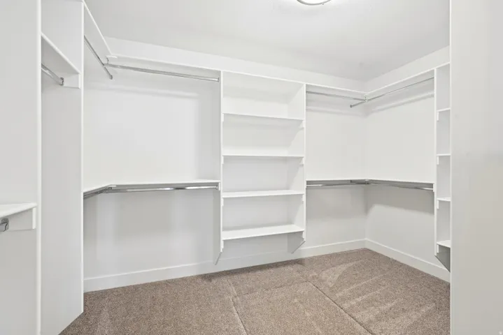 Built-in closet system featuring white shelving, multiple hanging rods, and recessed lighting