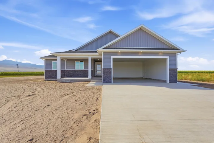 Single-story residence featuring light gray siding with dark stone accents, a covered front porch with white columns, a multi-pane front entry door, and an attached two-car garage with a concrete driveway