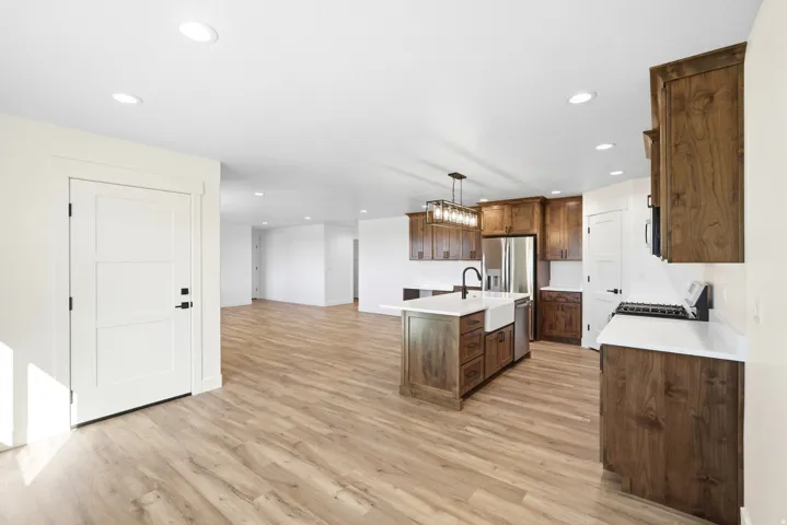Open-concept space featuring wood-finish flooring throughout, recessed lighting, and a kitchen with white countertops, dark wood cabinetry, and a central island with a farmhouse sink