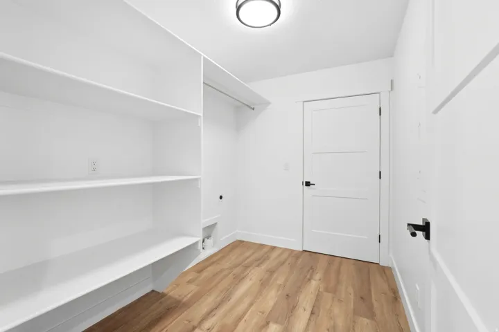 Wood-finish flooring, built-in shelving, panel doors with black hardware, ceiling light fixture, and a built-in hanging rod