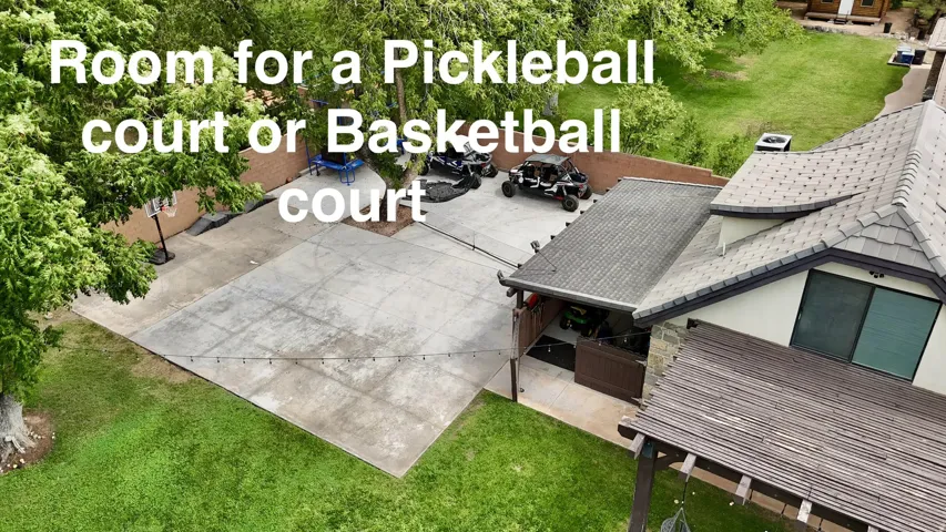 Expansive concrete hardscape with ample space for recreational courts, featuring mature landscaping and mature trees throughout the property
