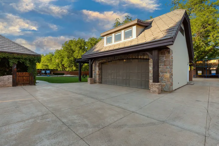 Detached garage structure featuring stone veneer accents, an arched garage door, and dormer windows