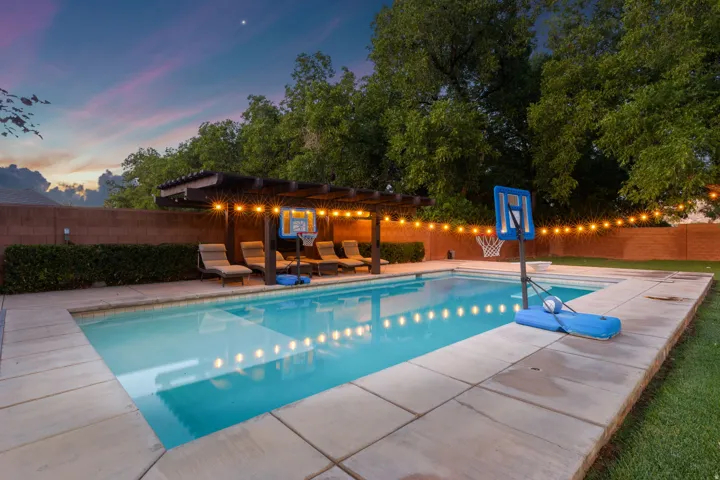 Resort-style backyard featuring a swimming pool, concrete decking, and a wood pergola with integrated lighting