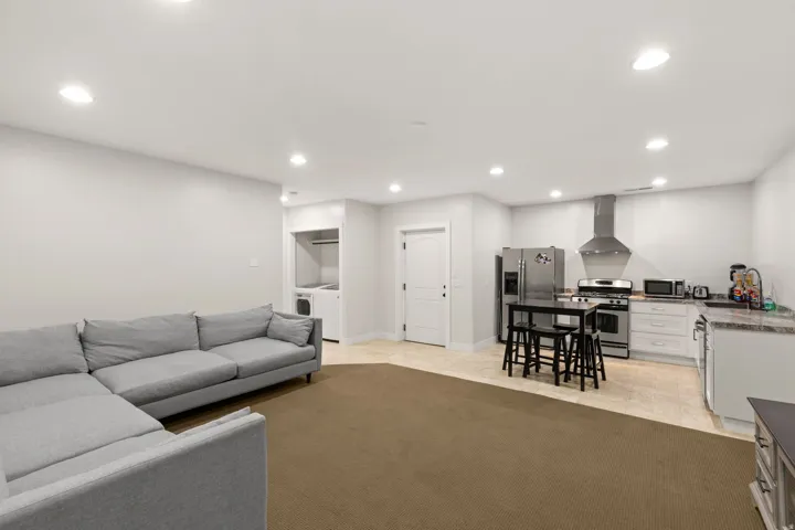 Open-concept living space featuring a full kitchen with stainless steel appliances, white cabinetry, and stone-finish countertops