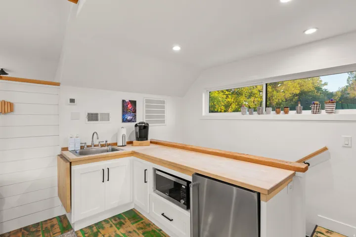Compact kitchenette featuring white shaker-style cabinetry, a stainless steel sink, and wood-finish countertops