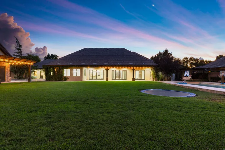 Expansive backyard featuring a manicured lawn, a large patio with exposed beam accents, and numerous sliding glass doors