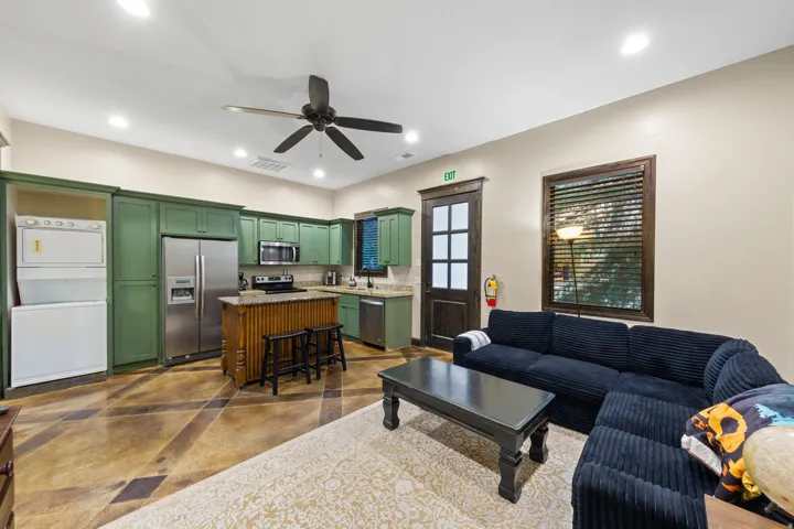 Open-concept living area featuring a full kitchen with green cabinetry, stainless steel appliances, and a central island