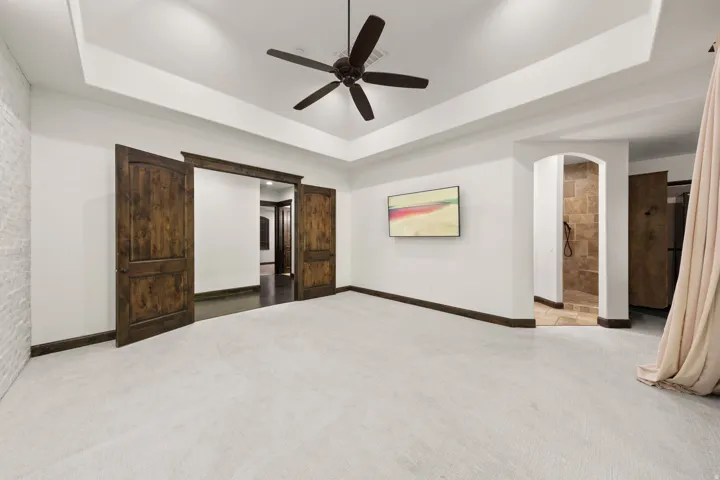Expansive interior space featuring light-colored carpeting and a tray ceiling with a dark ceiling fan