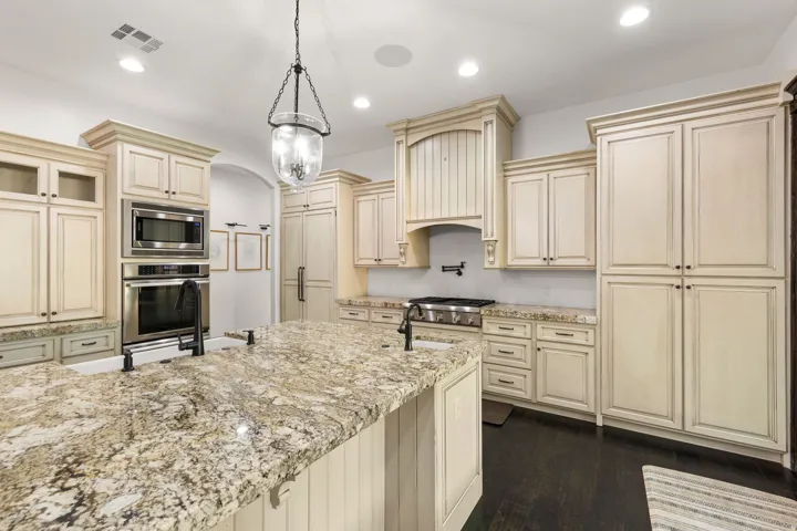 Spacious kitchen featuring a large island with a porcelain farmhouse sink, granite countertops, built-in stainless steel appliances, and abundant cream-finished cabinetry