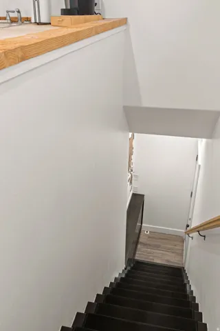 Staircase featuring dark carpeted treads and a natural wood handrail with matte black brackets