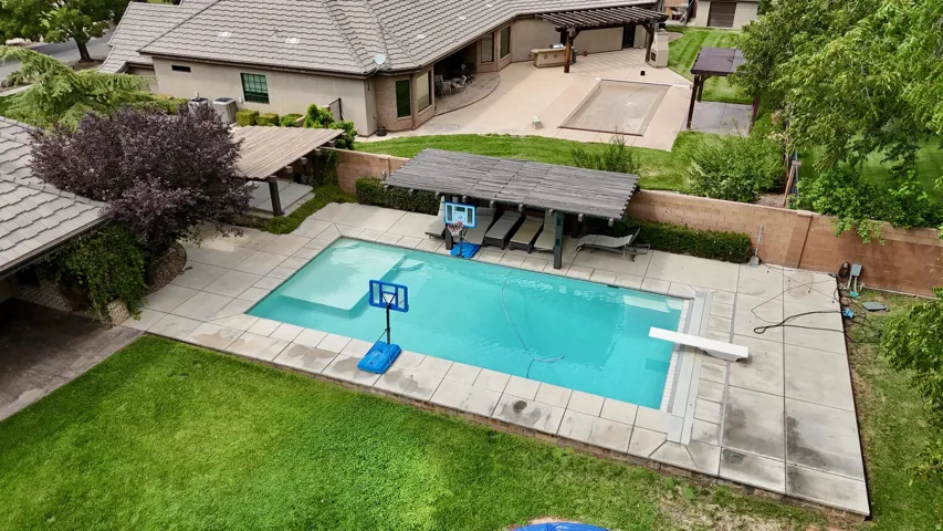 Resort-style backyard oasis featuring a sparkling in-ground swimming pool with integrated spa jets, surrounding paver decking, mature landscaping with privacy hedging, manicured lawn, and lounge seating areas