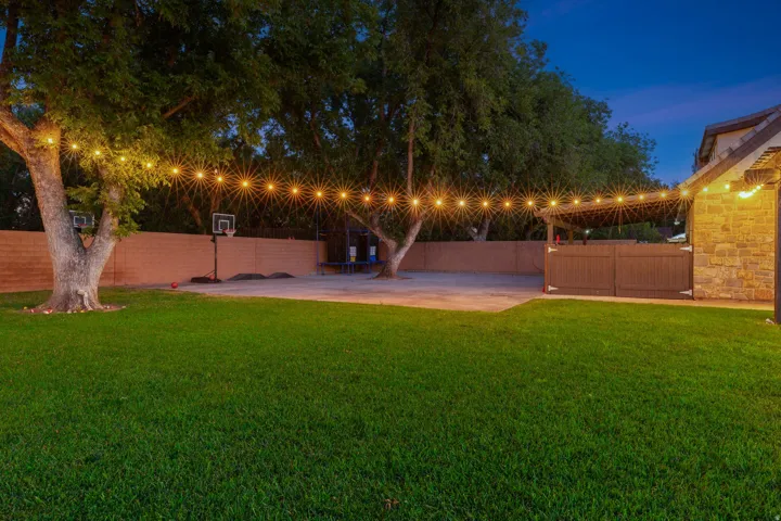 Expansive backyard featuring a lush lawn, mature trees, and a concrete patio