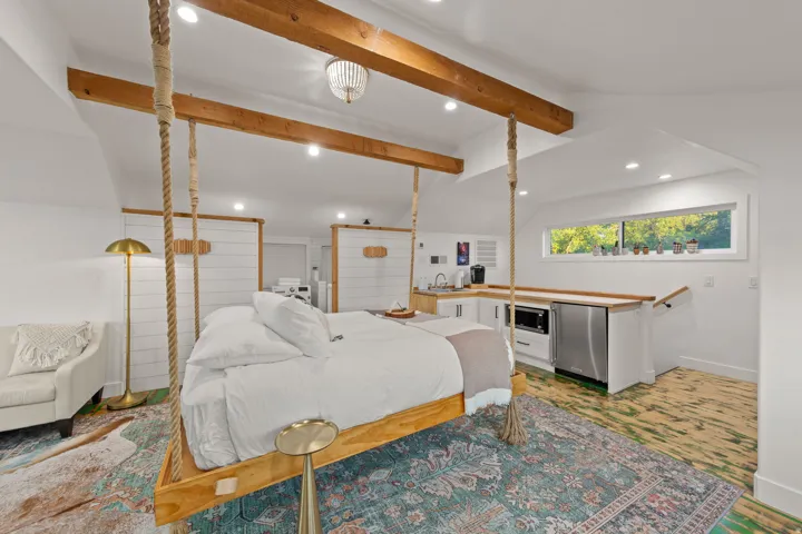 Open-concept living area featuring a hanging wood-frame bed, exposed wood beams, and recessed lighting