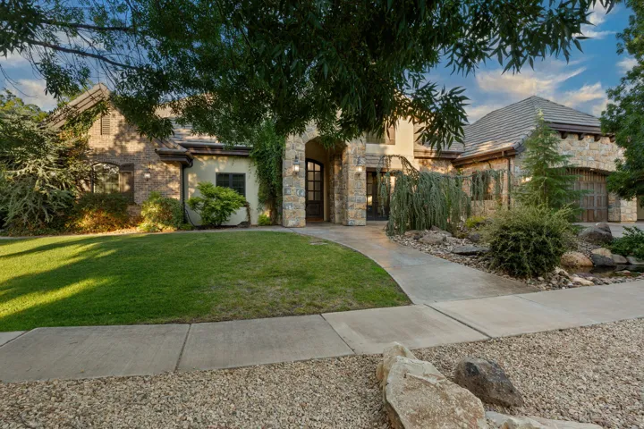 Stone and stucco exterior featuring a curved concrete walkway, mature landscaping, a stone archway entry, and an integrated garage
