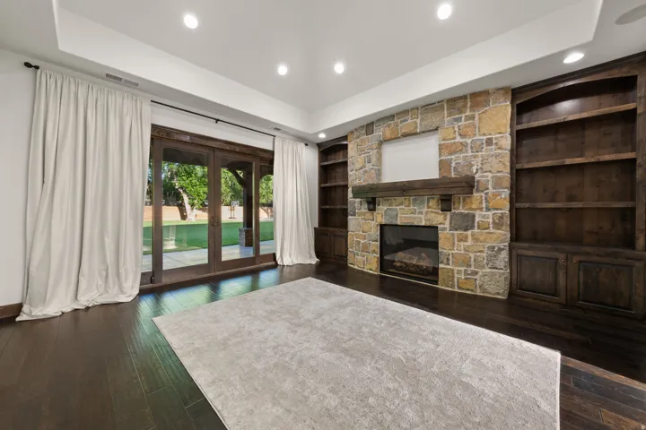 Spacious living area featuring dark wood-finish flooring and a stone-faced fireplace with a substantial wood mantel