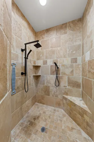 Spacious walk-in shower featuring large format wall tiles, a built-in corner bench, and integrated corner shelving