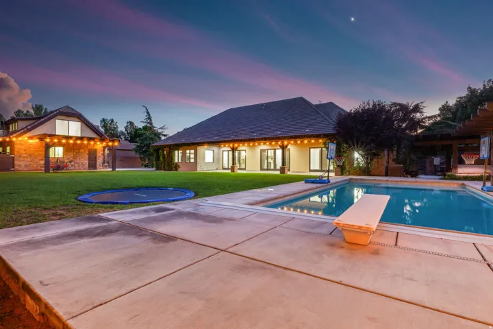 Expansive backyard featuring a swimming pool with a diving board, concrete surround, and perimeter lighting