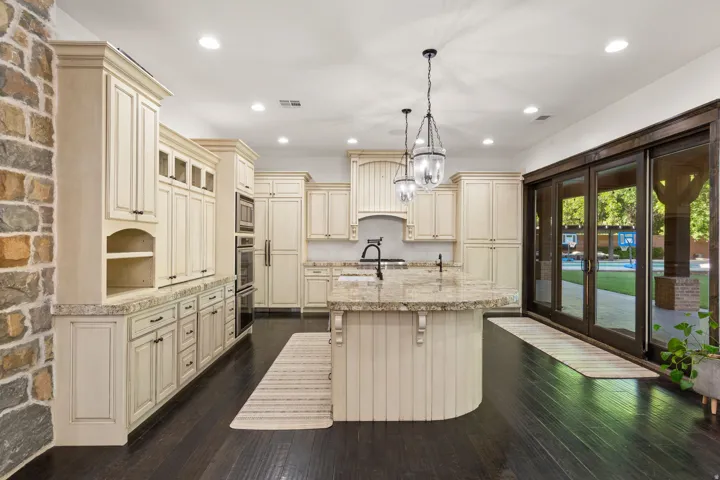 Gourmet kitchen featuring a large island, cream-colored cabinetry, stone countertops, double wall ovens, and wood-finish flooring