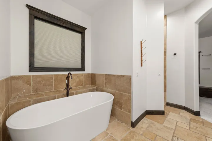 Freestanding oval soaking tub with a wall-mounted bronze-finish faucet, surrounded by natural stone tile wainscoting