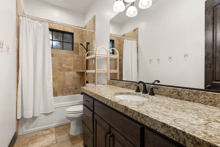 Bathroom featuring a granite countertop vanity with dark wood cabinetry, a large mirror, and a tub-shower combination