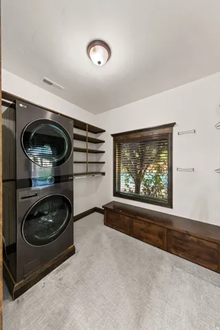 Dedicated laundry area with stacked washer and dryer unit, ample built-in shelving, a natural light window, and a wood-finish bench with integrated storage