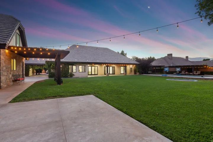 Expansive backyard featuring a manicured lawn, concrete patio, and string lighting