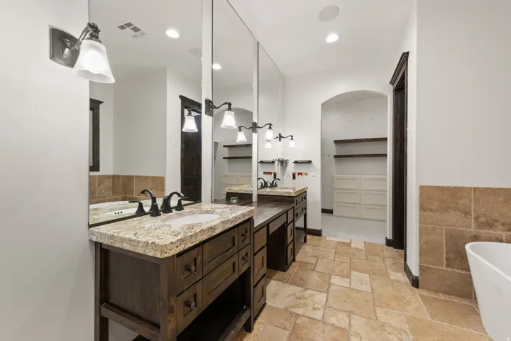 Expansive bathroom featuring dual wood-finish vanities with granite countertops, integrated sinks, and bronze-finish faucets