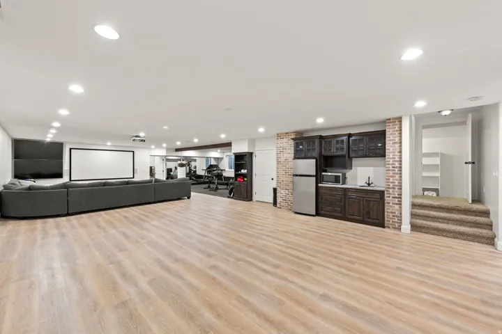 Spacious recreation room featuring light wood-finish flooring, recessed lighting, and a prominent media wall with projection screen