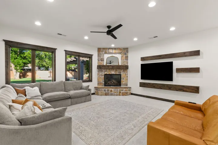 Spacious living area featuring a corner stone fireplace with a wood mantel, dark wood trim around windows, and a built-in entertainment wall with floating wood shelves