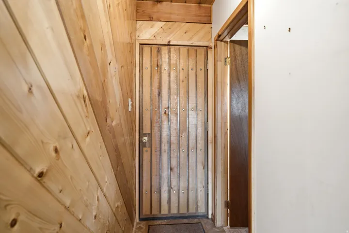 FRONT DOOR. Wood-paneled interior wall with a vertical wood plank door featuring decorative metal accents