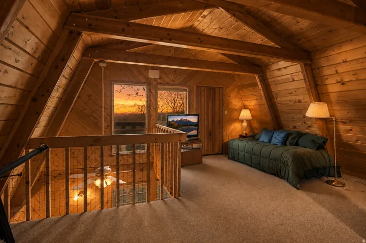 Loft space featuring vaulted wood-paneled ceilings with exposed beams, carpeted flooring, and a natural wood railing overlooking the floor below