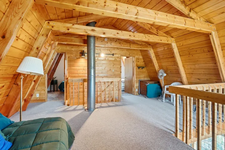 Carpeted loft area featuring exposed wood beams and paneling, a wood railing with metal infill, and a dark metal support column