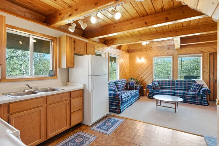 Rustic cabin interior showcasing exposed beam wood ceiling with recessed lighting, wood-paneled walls, and expansive windows framing natural surroundings