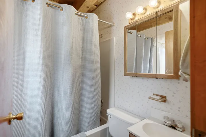Bathroom featuring a wooden vanity mirror with integrated lighting, a white ceramic sink, and patterned wallpaper
