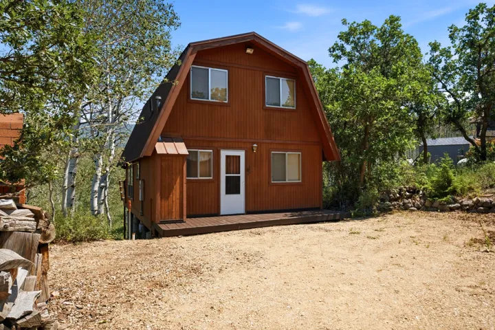 Barn-style dwelling featuring a light brown exterior finish, dark shingle roof, and multiple white-framed windows